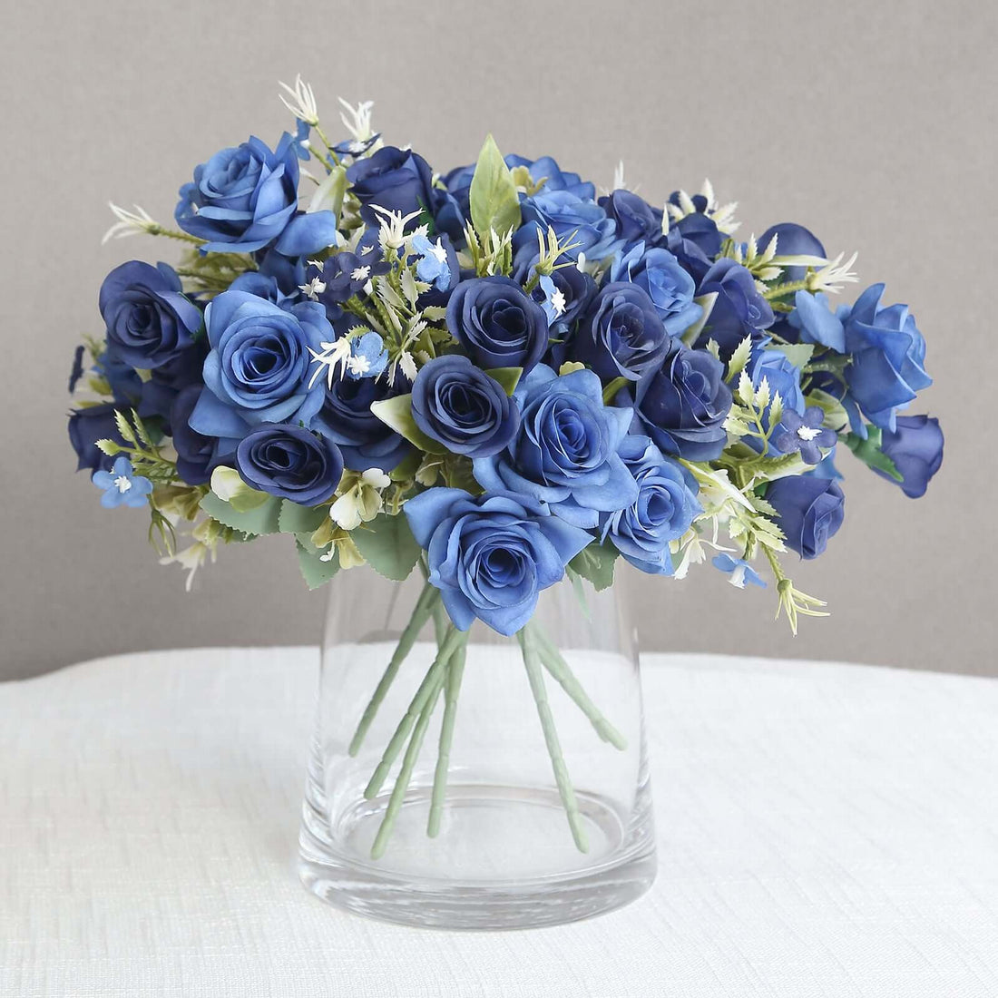 Blue rose bouquet in a clear glass vase on a neutral background.