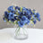 Blue rose bouquet in a clear glass vase on a neutral background.
