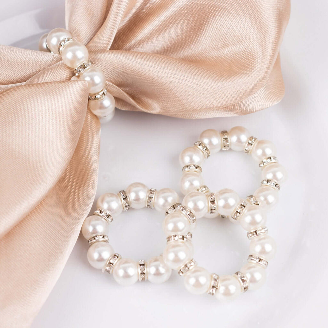 Elegant pearl napkin rings with silver accents on a silk napkin.