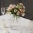 Artificial flower bouquet in a clear glass vase on a dining table.
