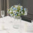 Blue rose bouquet in a clear vase on a dining table setting.
