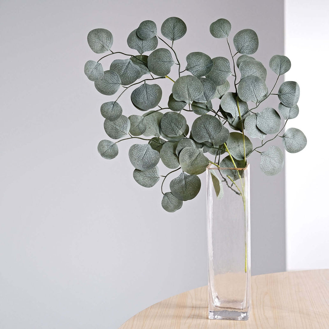 Eucalyptus branches in a clear vase on a wooden table.