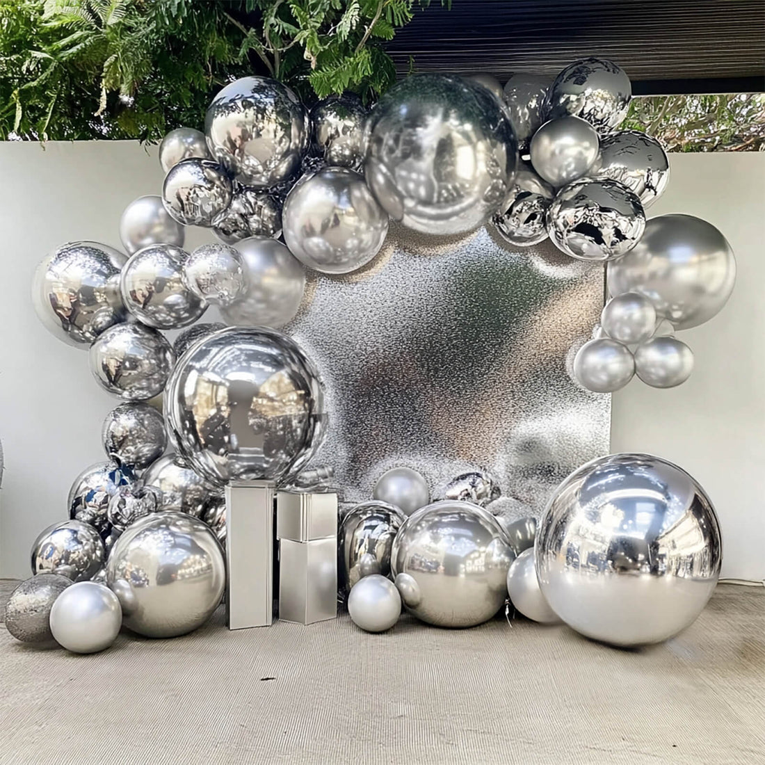 Silver balloon arch decoration with reflective spheres and backdrop.