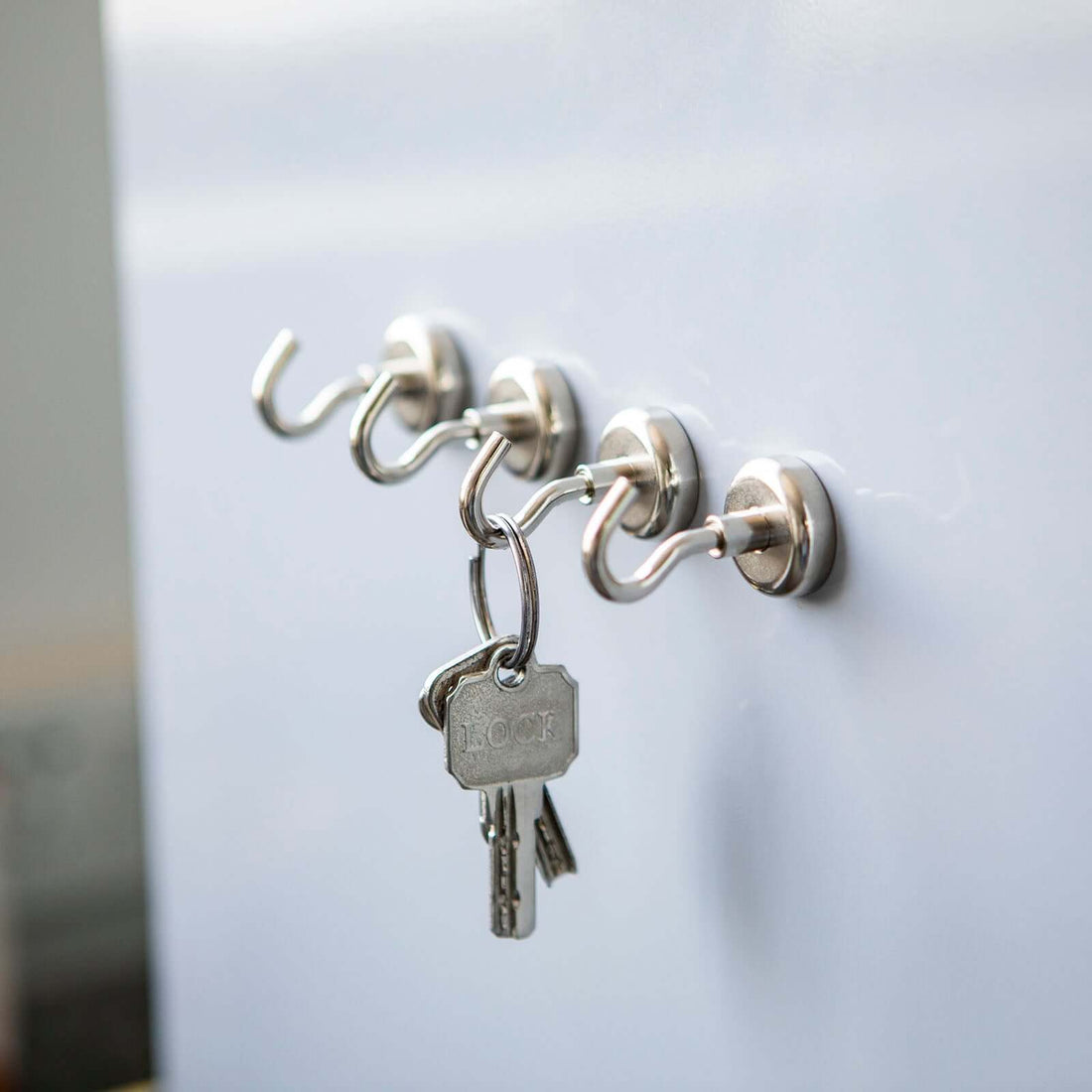 Metal key hooks with keys hanging on a white wall.