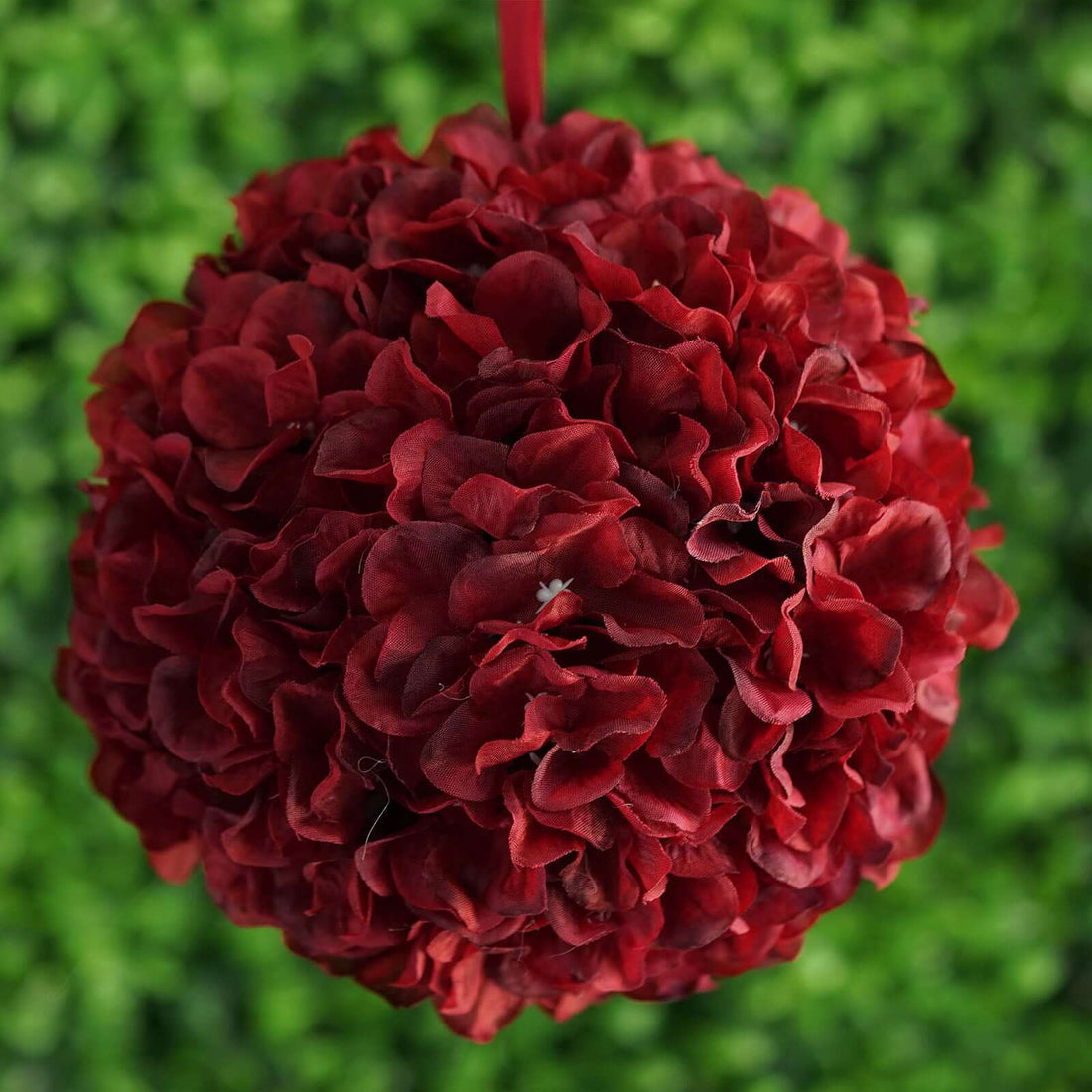 Red floral ball decoration hanging against green background.