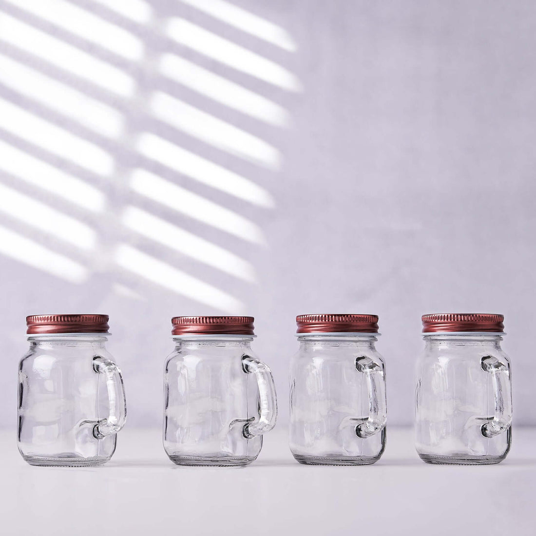 Set of four glass jars with handles and red lids.