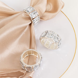 Elegant silver rings with clear gemstones displayed on a silk napkin.