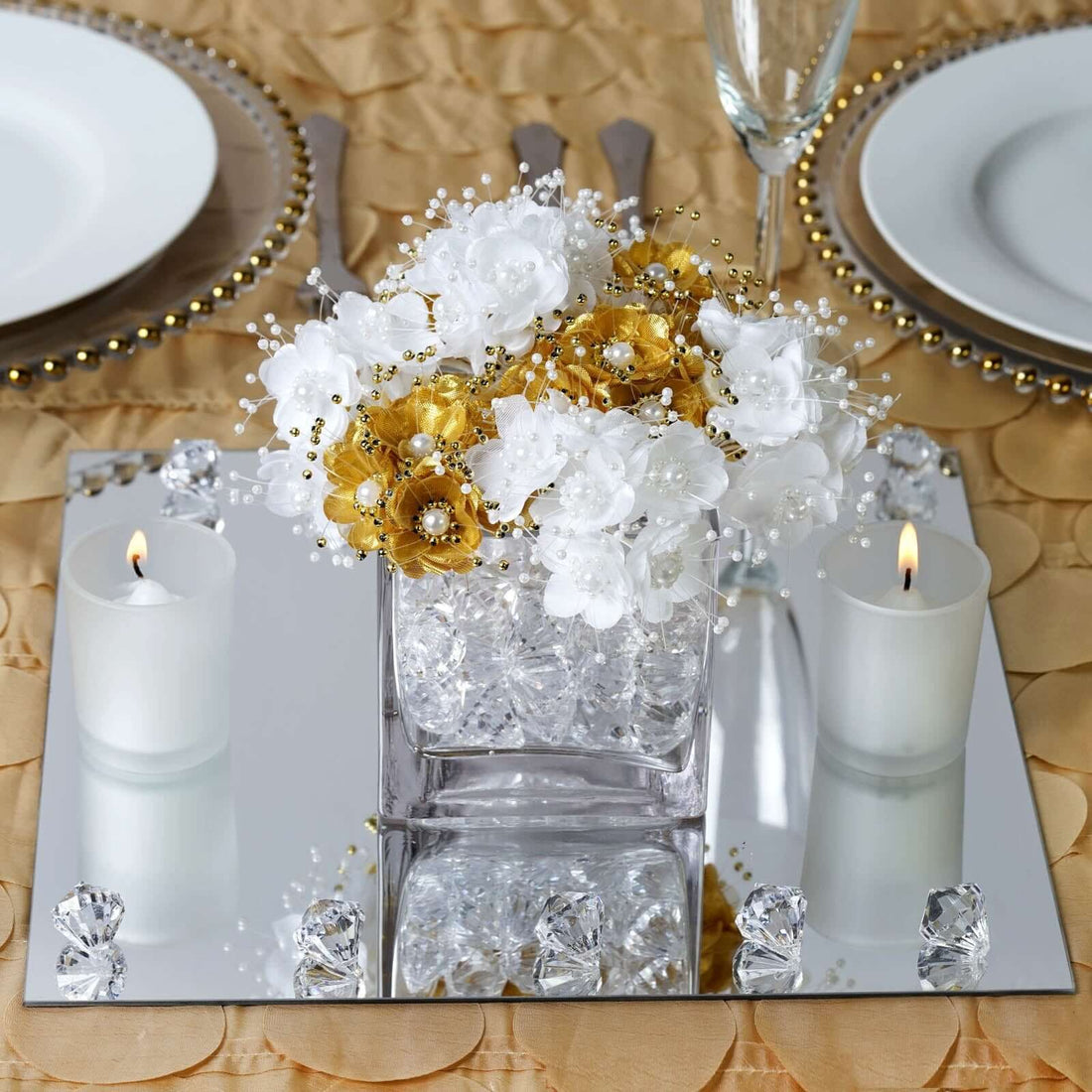 Elegant floral centerpiece with white and gold flowers, candles, and mirrored base.