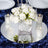 Elegant white rose centerpiece with candles on a reflective surface.
