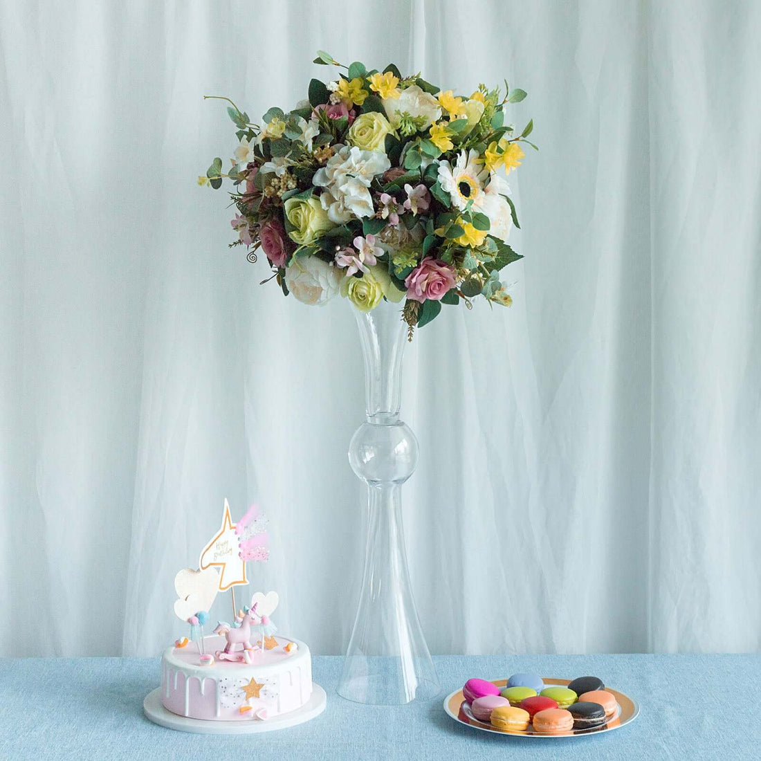 Floral arrangement in a vase with a cake and colorful macarons on a table.
