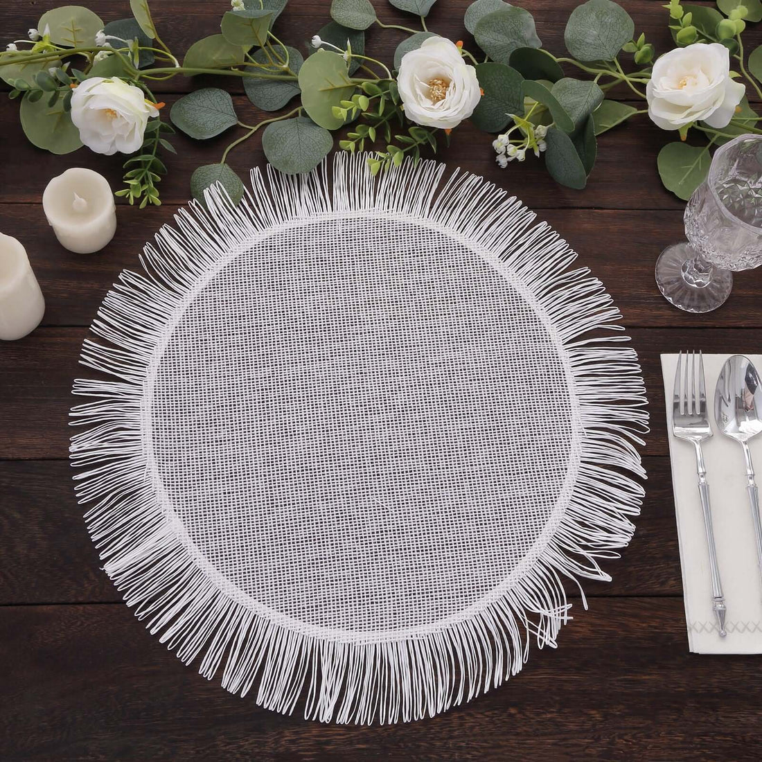 White fringed placemat surrounded by greenery and candles.