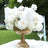 Elegant white rose centerpiece in a gold vase with feathers, set outdoors.