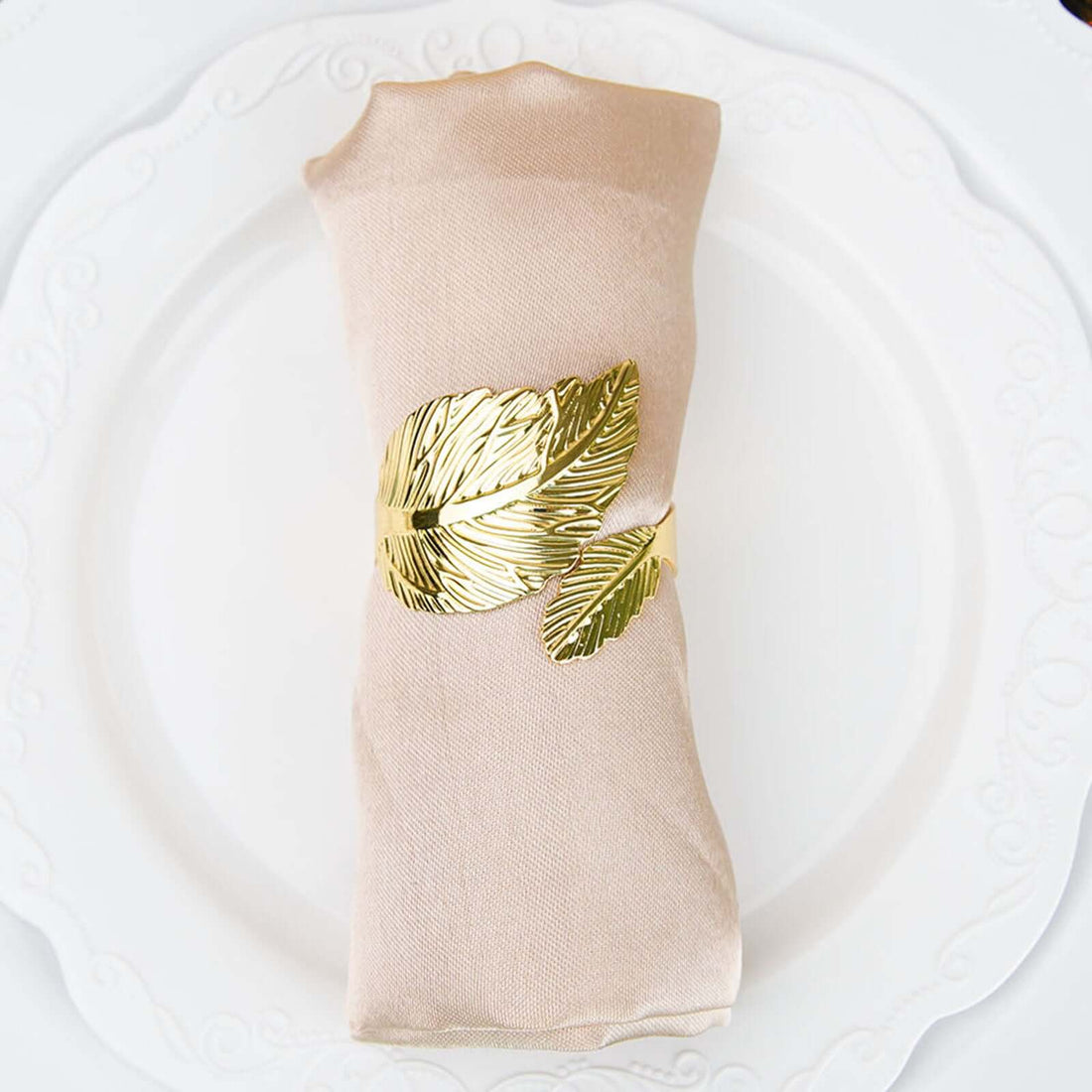 Gold leaf napkin ring on a beige napkin placed on a white plate.