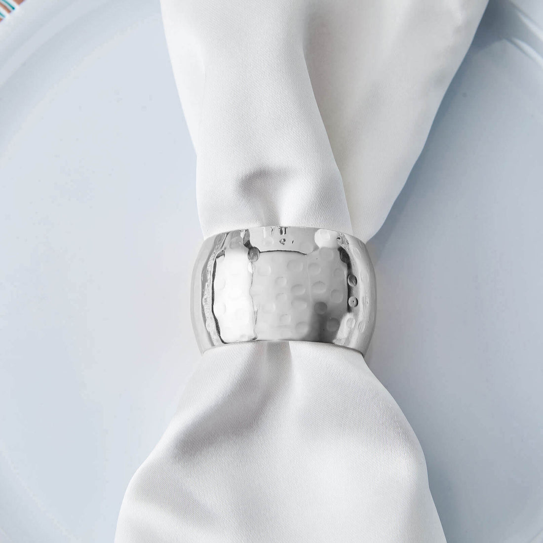 Silver napkin ring on a white napkin atop a plate.