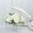 White roses in a glass vase with a white parasol on a table.