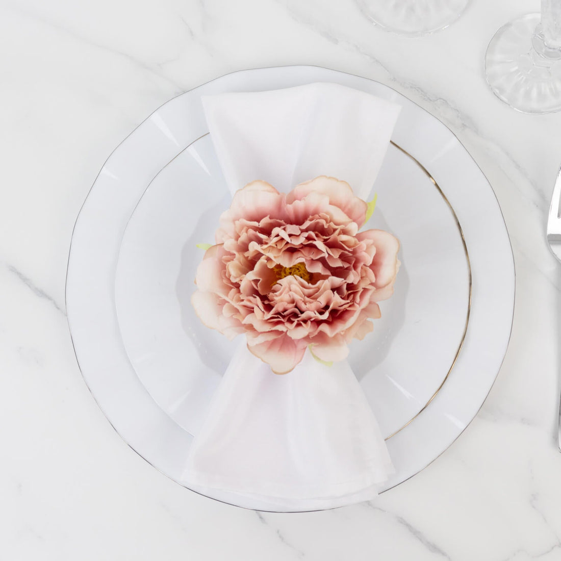Elegant pink flower on a white plate setting with a napkin.