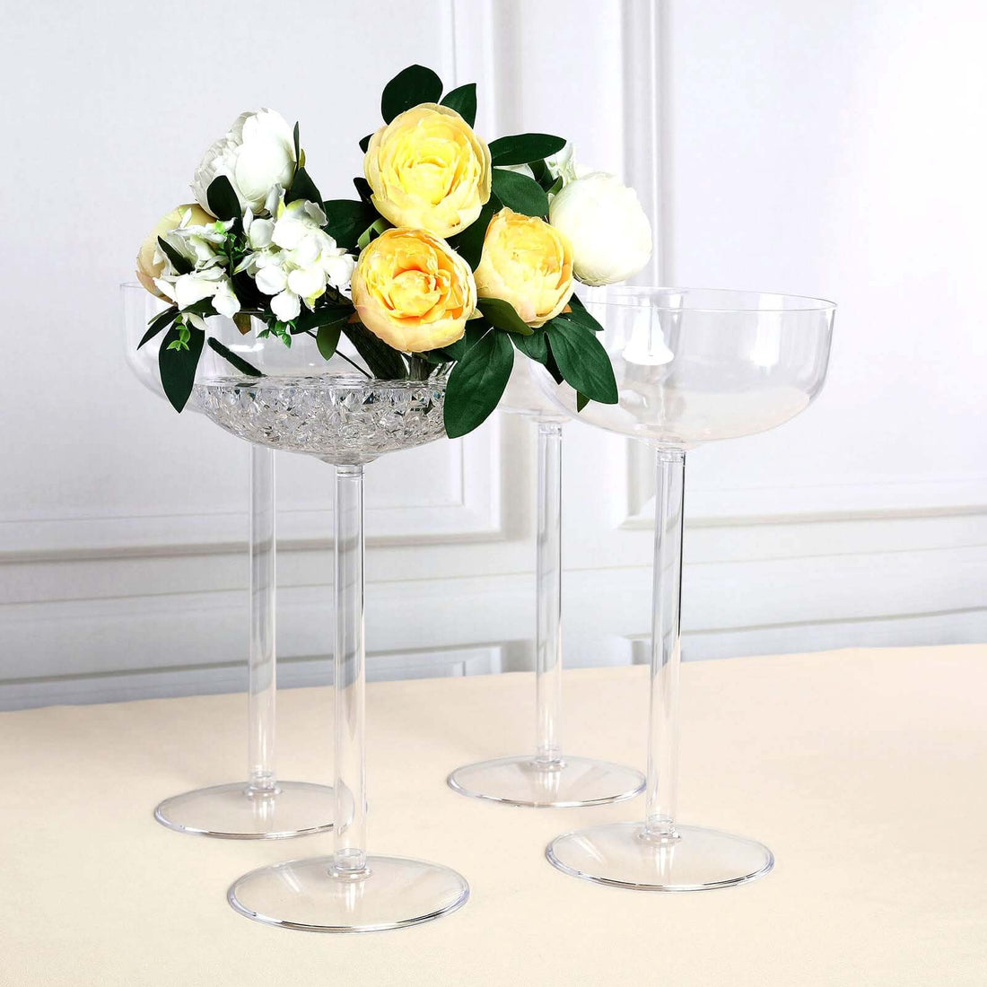 Clear crystal flower vases with yellow and white roses on a neutral background.