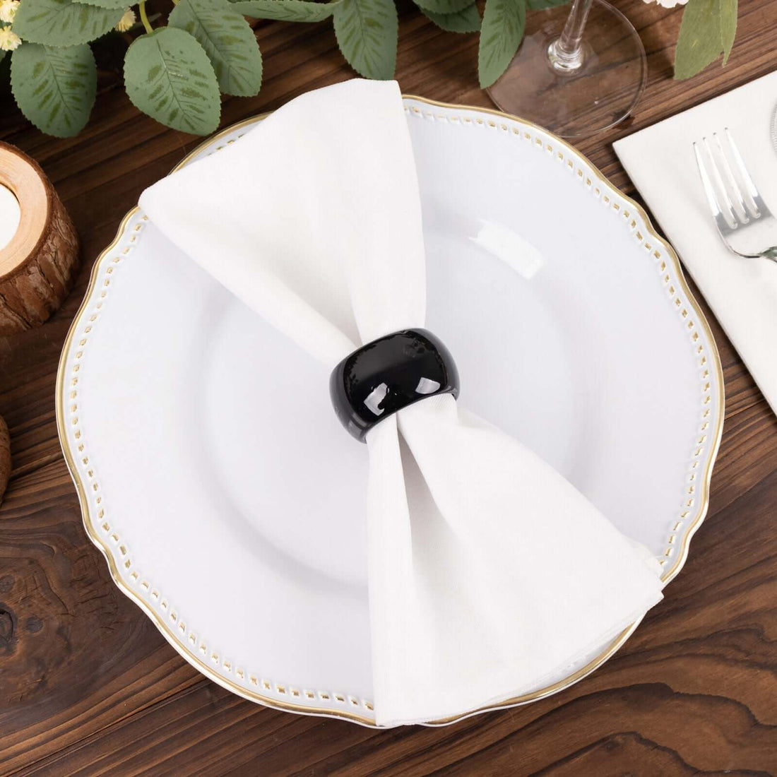Elegant white napkin with black napkin ring on a decorative plate.