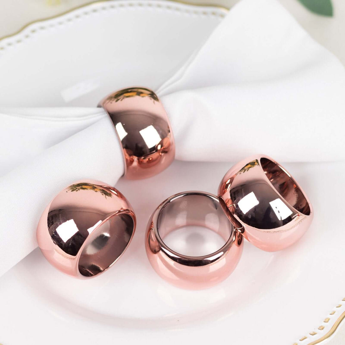 Rose gold napkin rings set on a white plate with a napkin.