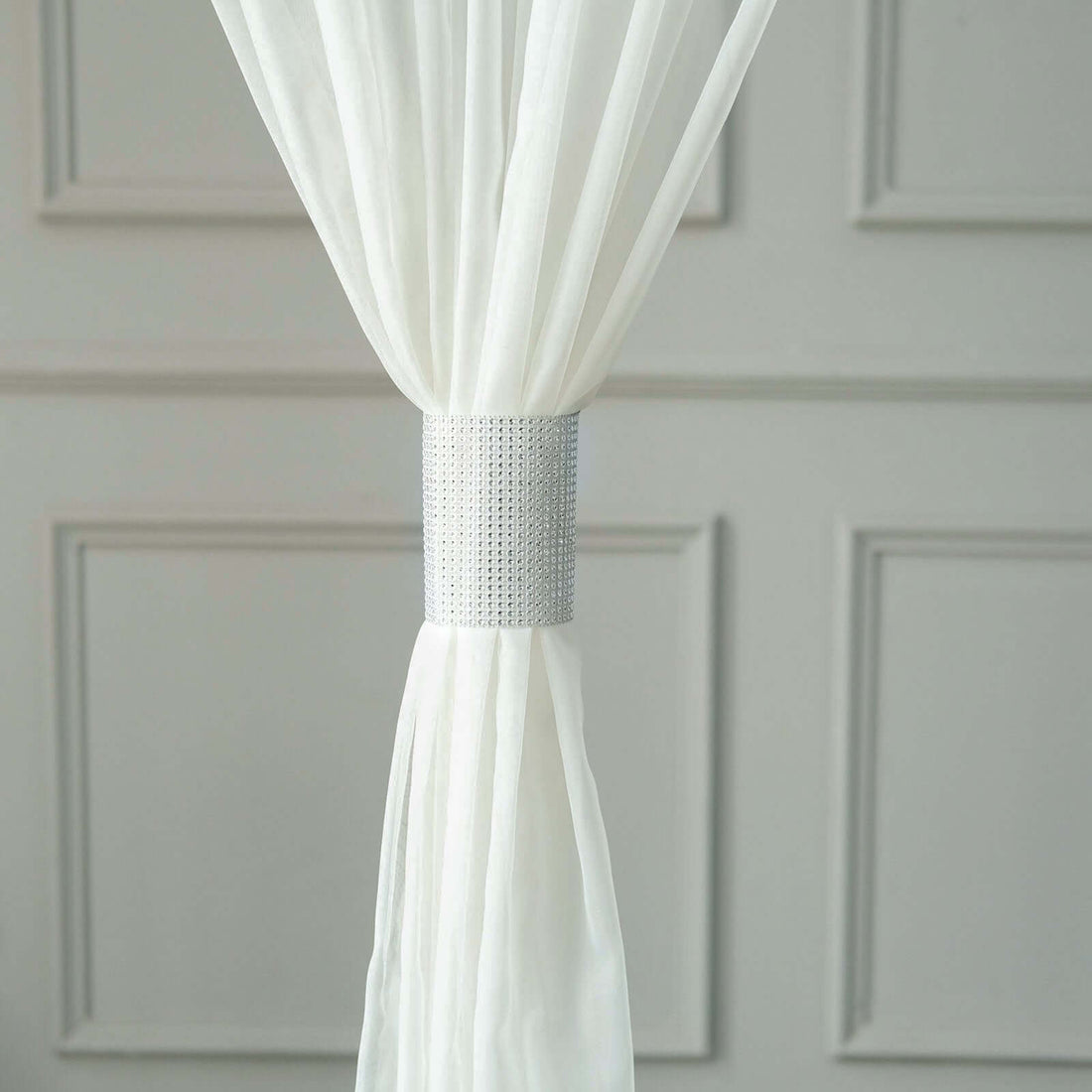 White curtain held with a silver decorative tieback.