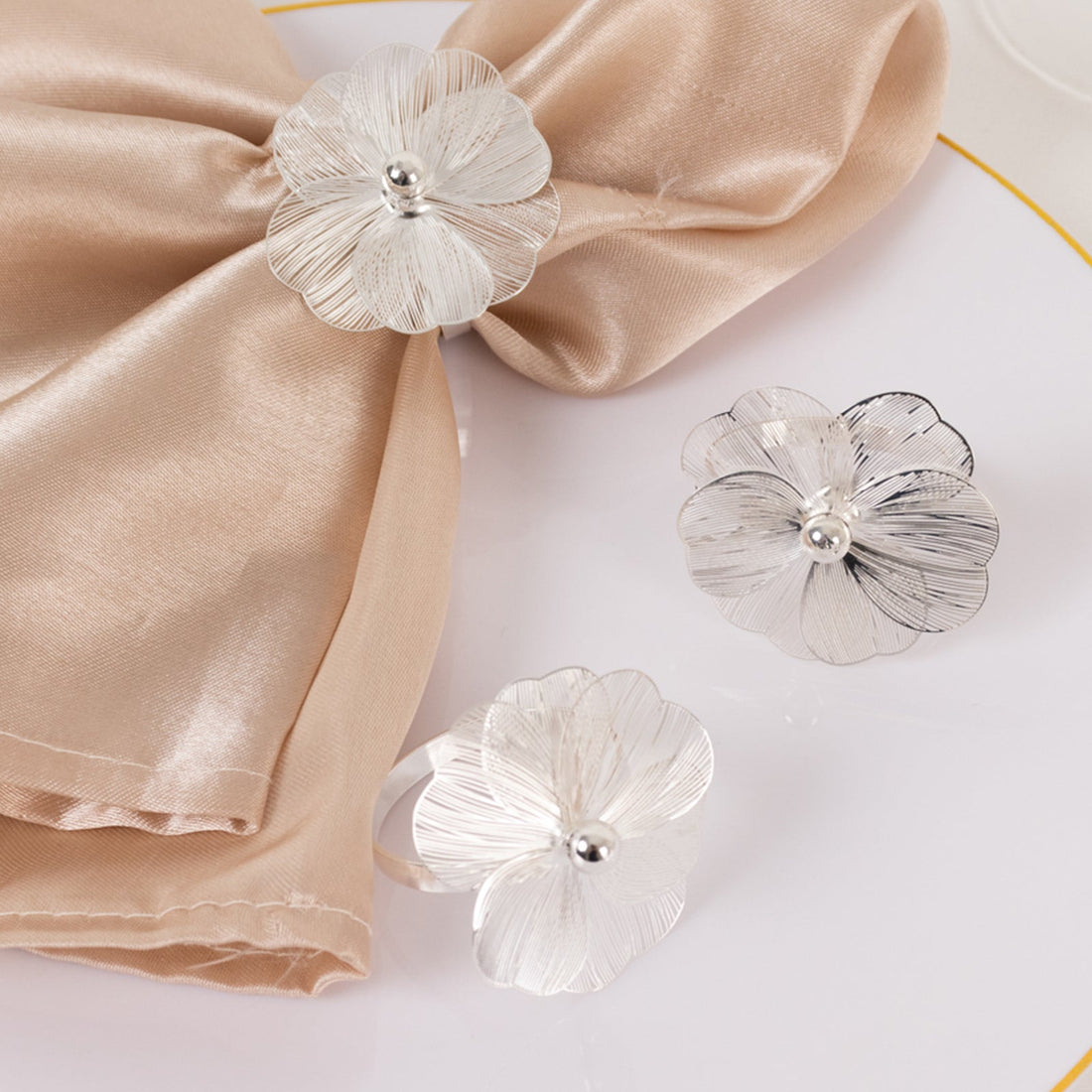 Silver flower napkin rings elegantly displayed on a silk napkin.