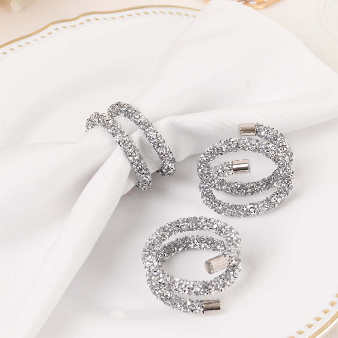 Silver glitter napkin rings on a white table setting.