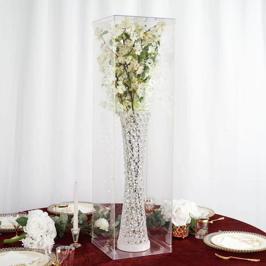 Crystal vase with flowers in a clear display box on a table setting.