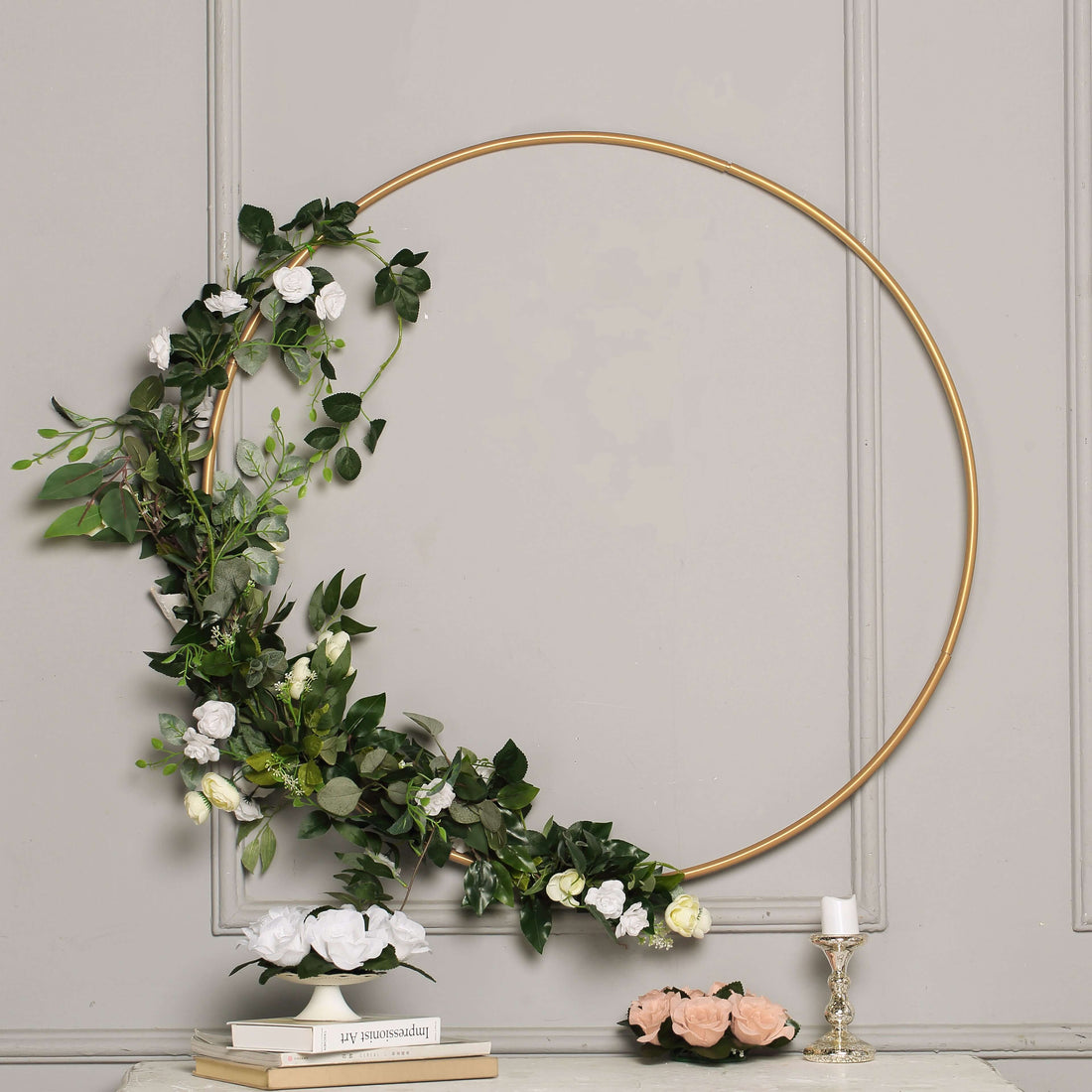 Decorative floral hoop with greenery and white flowers on a gray wall.