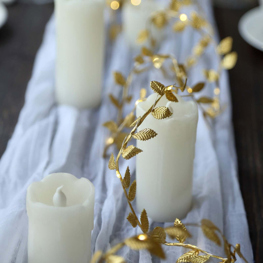 White candles with gold leaf garland on a table setting.