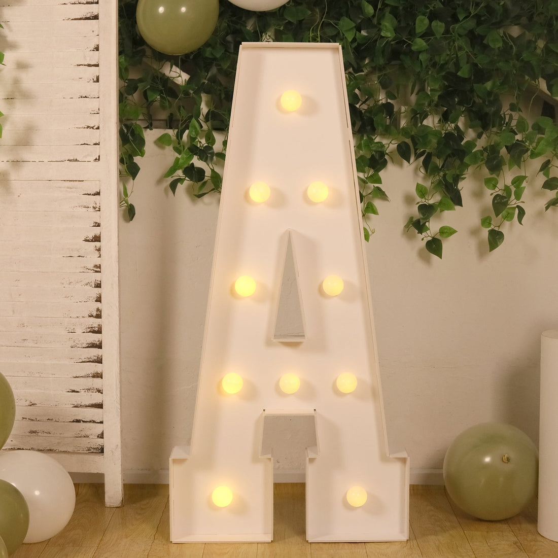 Illuminated marquee letter A with balloons and greenery backdrop