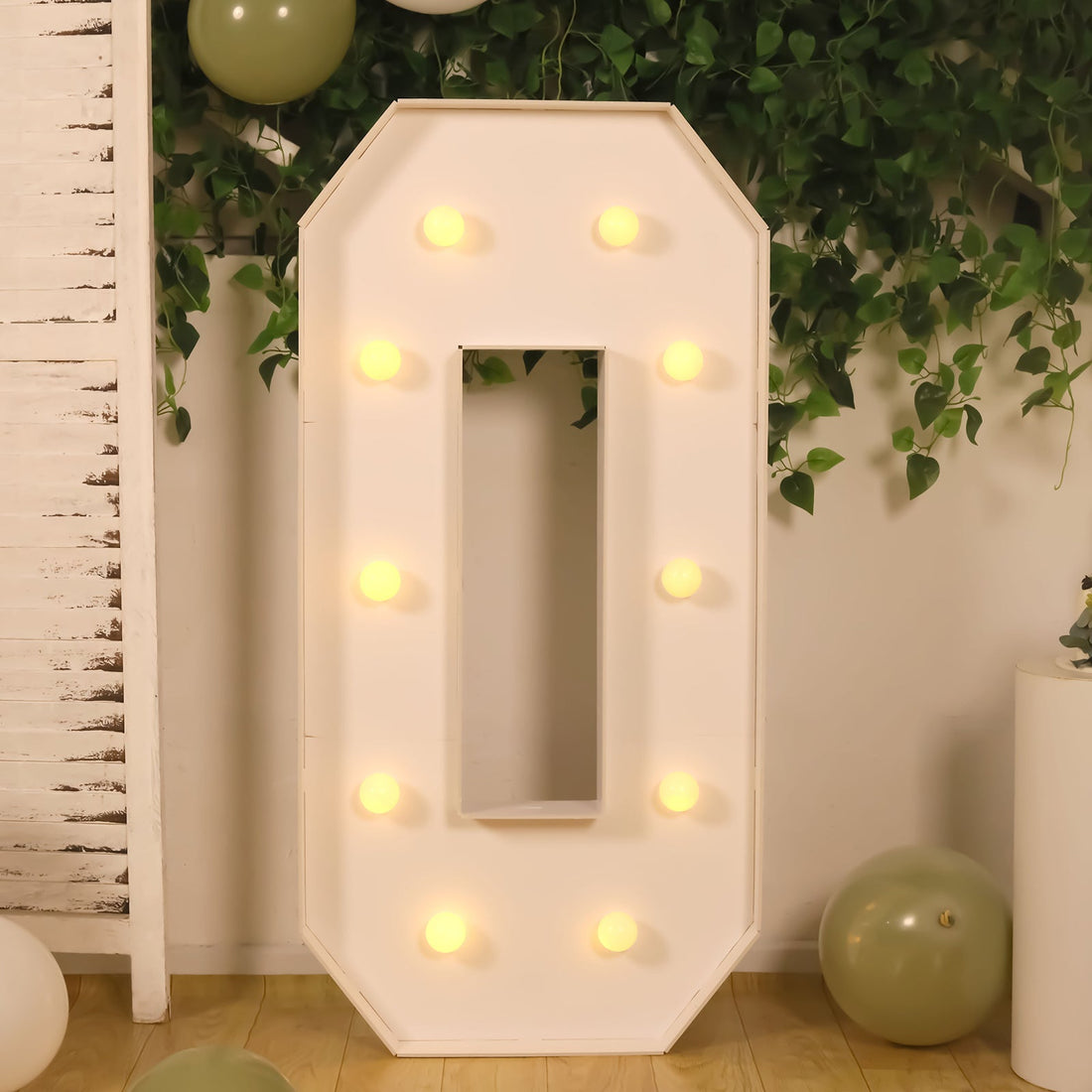 Light-up marquee number zero in a decorative setting with greenery and balloons.