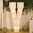 Illuminated letter V sign with lights, surrounded by greenery and balloons.