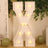 Light-up marquee letter "X" in white with bulbs, set against greenery and balloons.