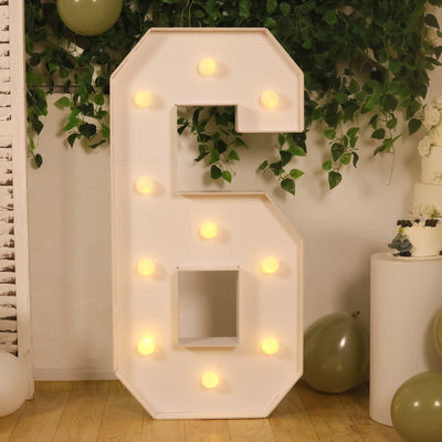 Lit marquee letter S with warm bulbs and greenery backdrop