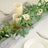 Candle centerpiece with greenery and flowers on a table setting.