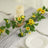 Yellow flowers and candles arranged on a table with plates and utensils.
