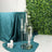 Elegant glass candle holders with white candles on a teal tablecloth.