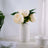 White vase with faux peonies on a table, soft natural decor.