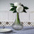 Clear glass vase with white peony flowers and green leaves.