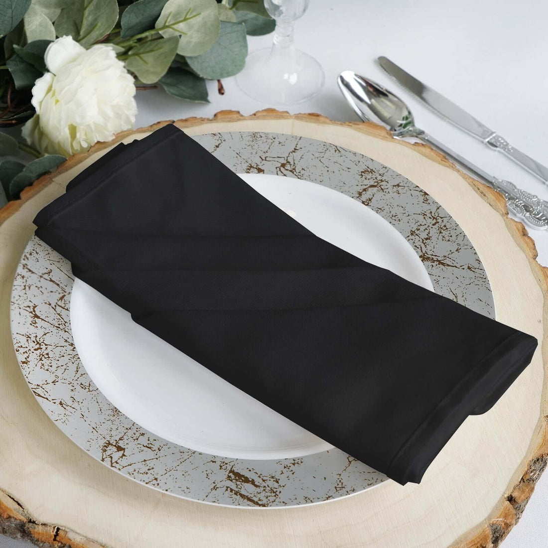 Black napkin elegantly arranged on a decorative plate with a rustic wooden base.