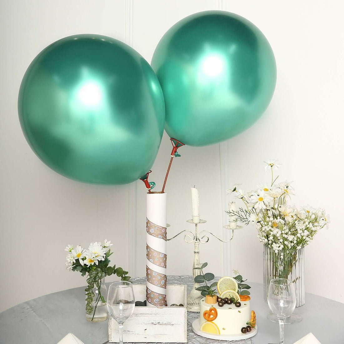 Green metallic balloons with a cake and flowers on a table setting.