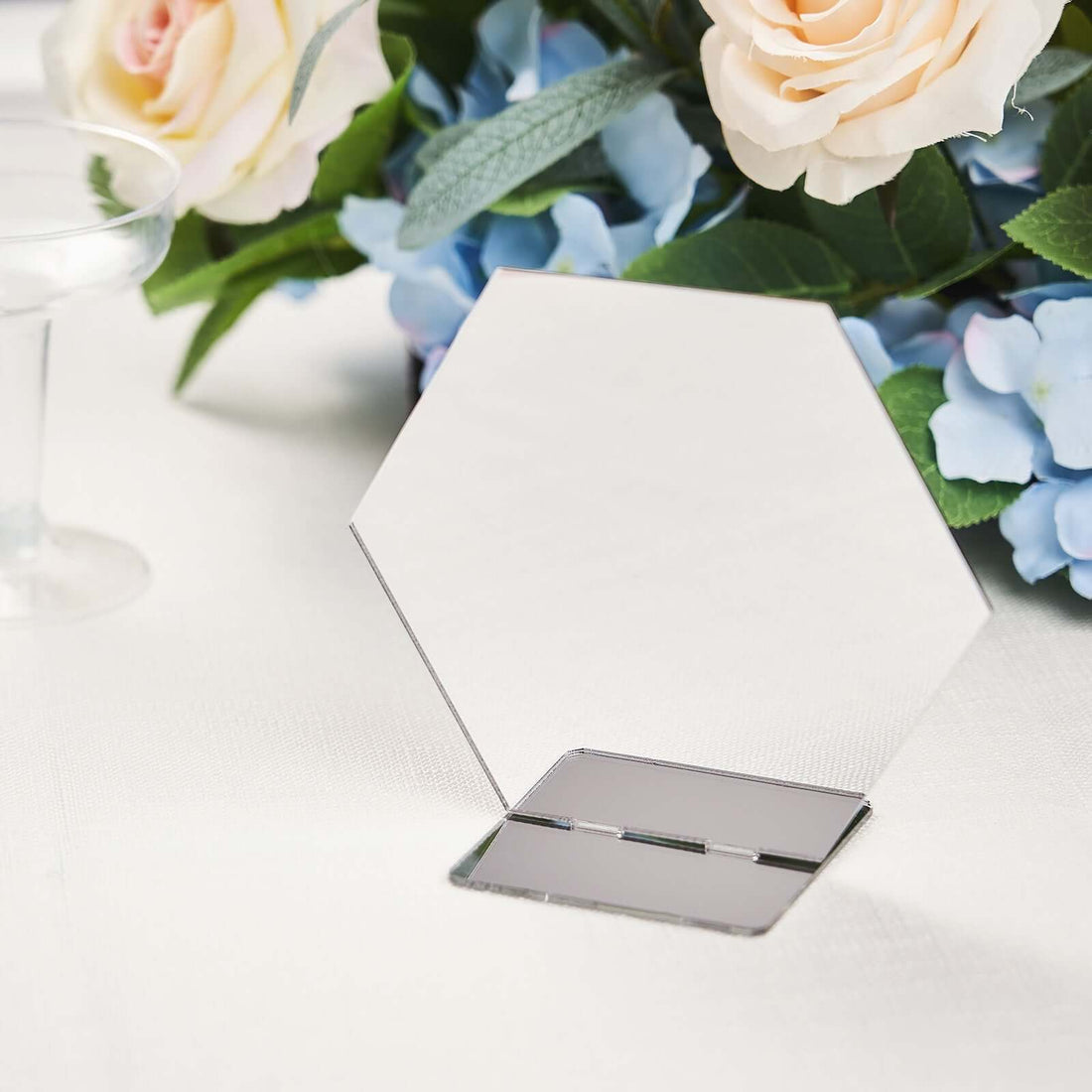 Hexagonal mirror with a stand, elegantly displayed near floral decor.