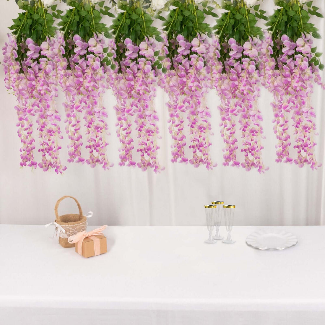 Decorative pink flower garlands with a gift box and champagne glasses on a table.