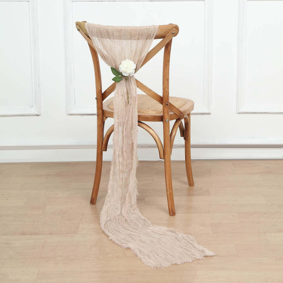 Neutral linen chair tie with white flower decoration on a wooden chair.