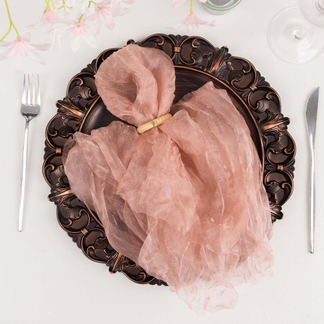 Pink sheer napkin elegantly tied with a wooden ring on a decorative plate.