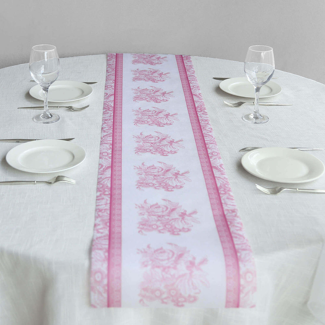 Pink floral table runner on a round dining table with plates and glasses.