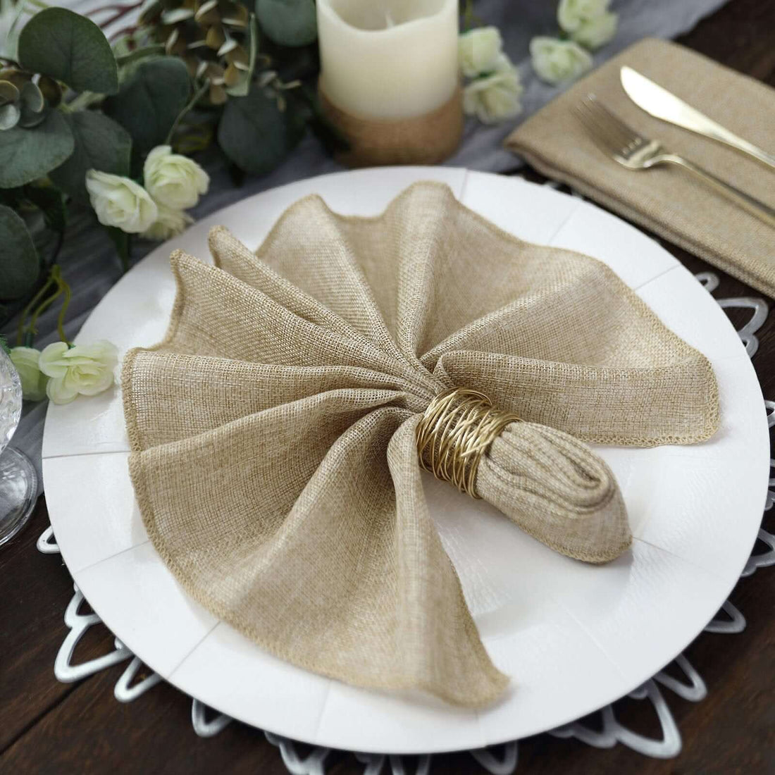 Elegant beige linen napkin elegantly folded on a white plate with gold utensils.