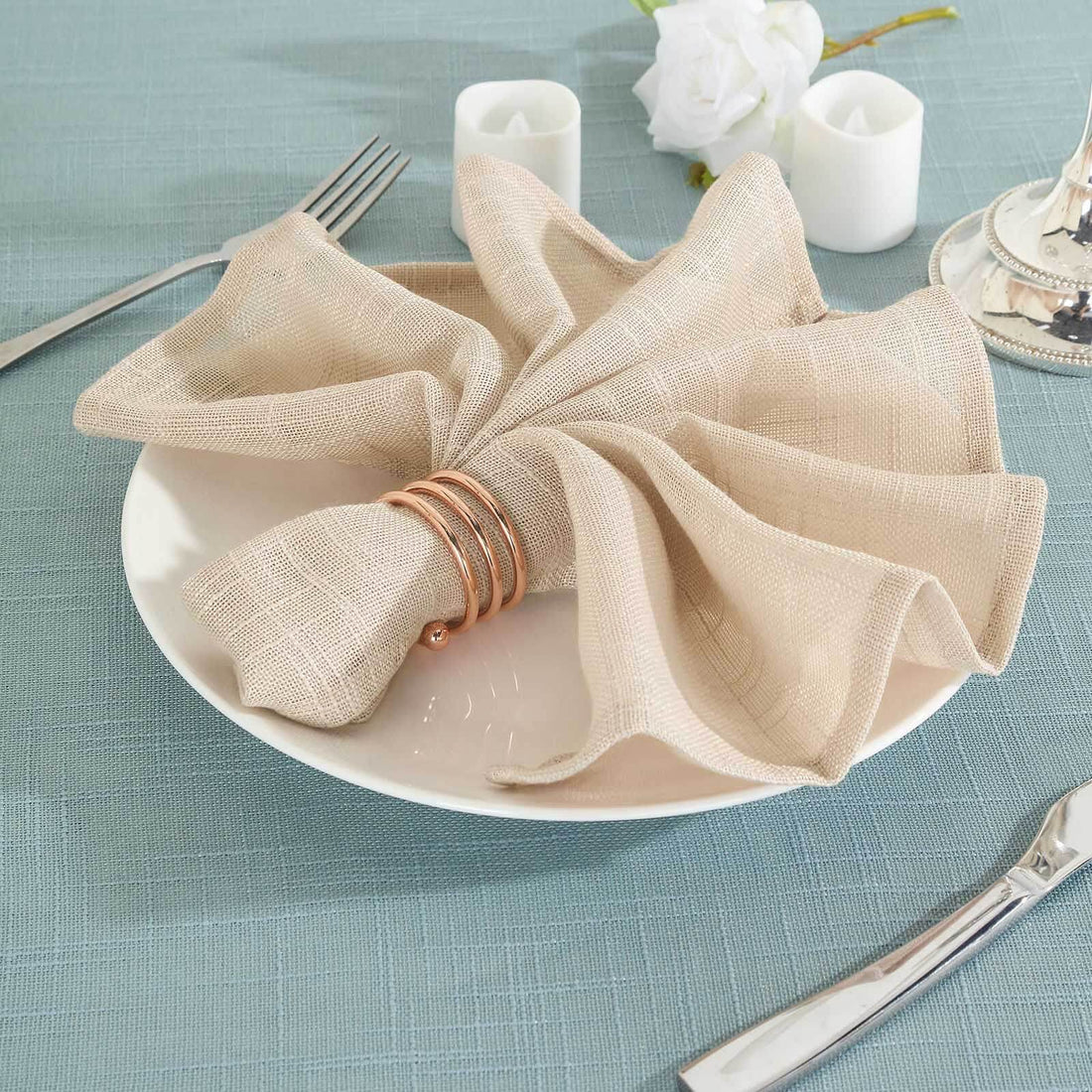 Beige napkin elegantly arranged on a plate with decorative rings and simple table setting.