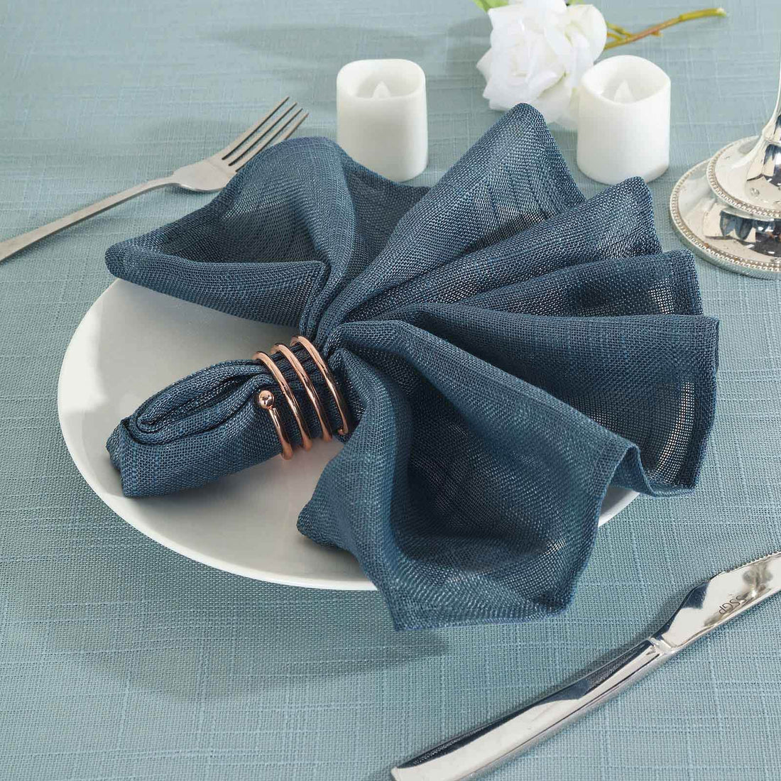 Navy blue napkin elegantly arranged on a white plate with silver cutlery.
