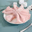 Pink linen napkin elegantly arranged on a white plate with silver cutlery and candles.